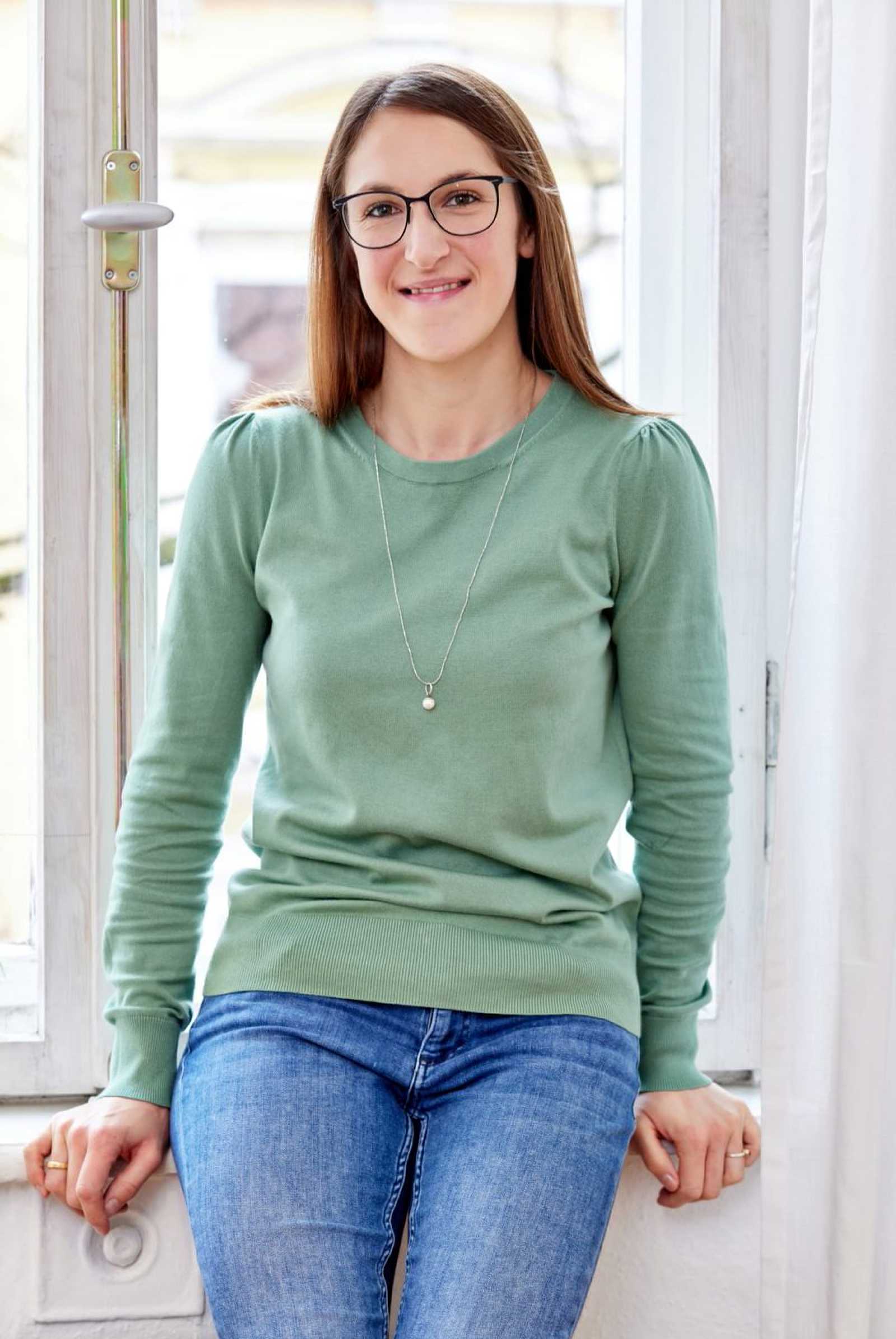 Psychotherapeutin Katharina Stephan auf dem weißen Fensterbrett sitzend lächelt freundlich in die Kamera